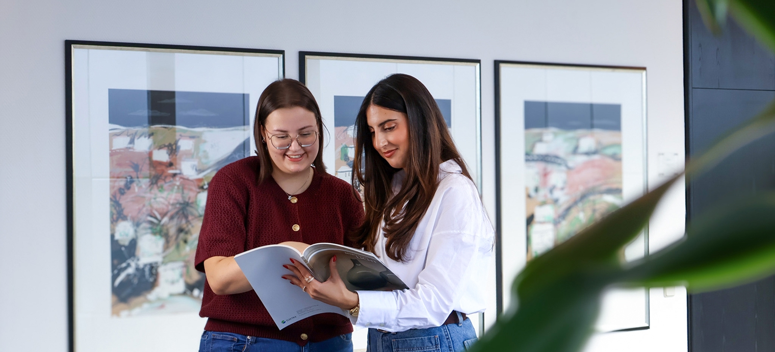Zwei Frauen betrachten ein Buch in einer modernen Umgebung.