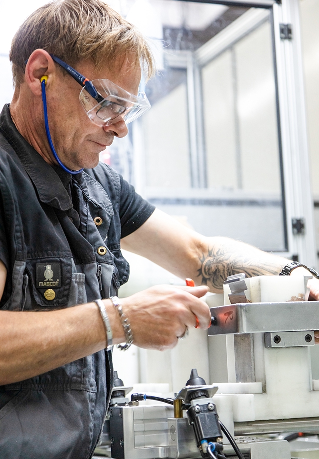 Mann mit Tätowierung und Armband arbeitet an einer Maschine in einer Produktionsumgebung